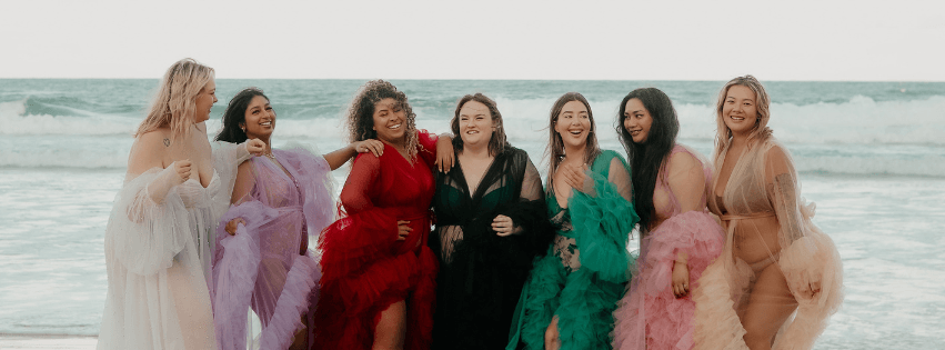 A group of models pose on a beach. They are smiling.