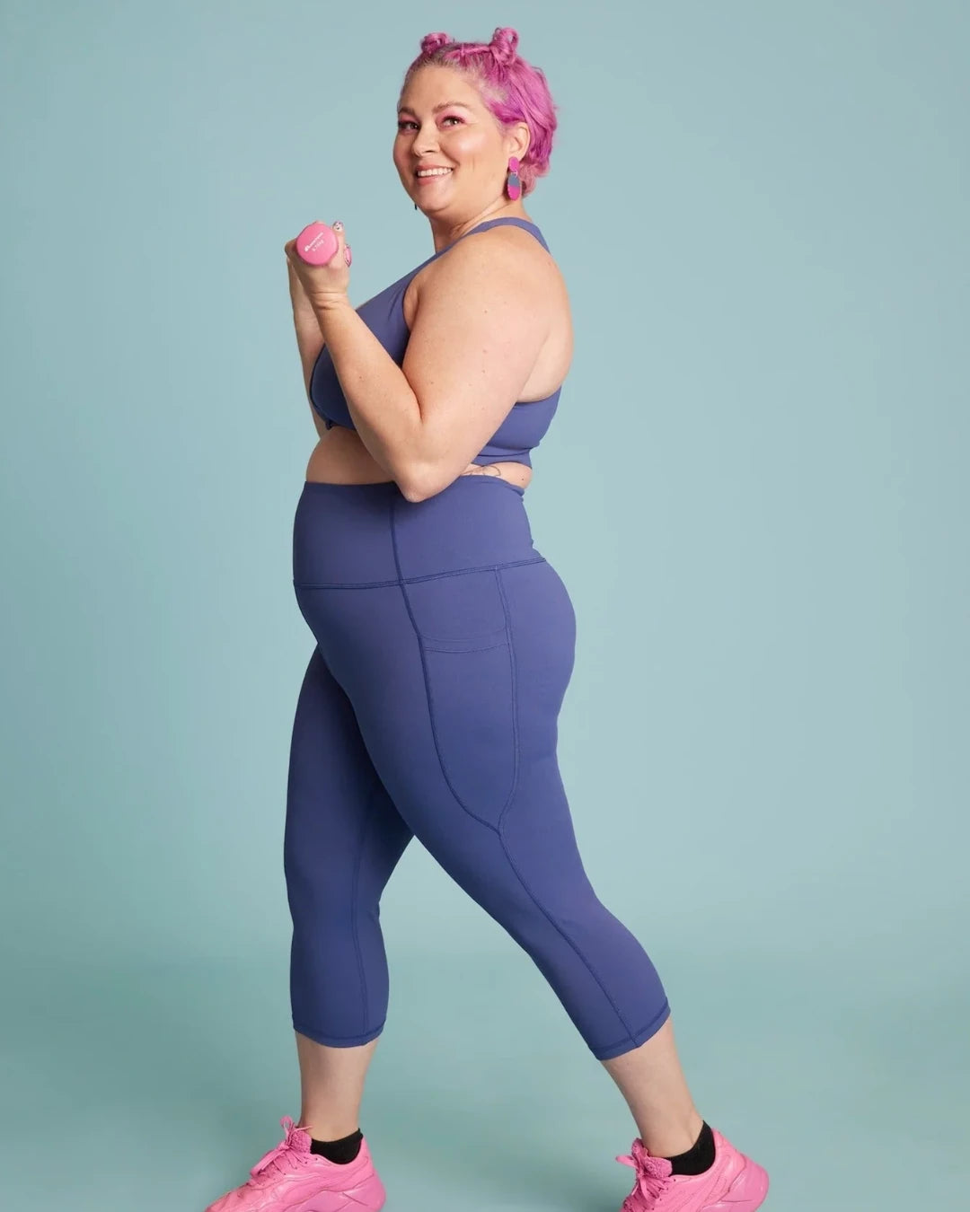 Plus size woman poses in matching purple leggings and crop top